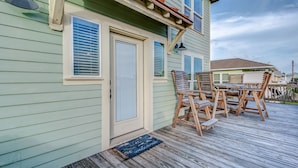A wooden deck with a table and chairs, a door with a window, and a welcome mat.