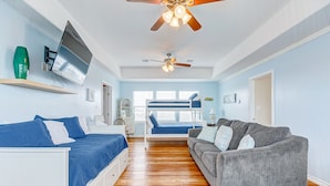 A bedroom with a bed, a gray sofa, a TV mounted on the wall, and a ceiling fan.