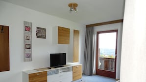 A modern living room with a flat-screen TV on a wooden cabinet, a patterned rug, and a balcony with a view. - Cozy apartment on the farm Vöran / Hafling (Vöran)