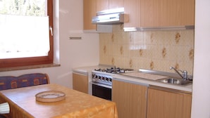 A compact kitchen with a gas stove, oven, and a sink. There is a window providing natural light and a table with a tablecloth. - Cozy apartment on the farm Vöran / Hafling (Vöran)