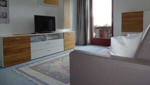 A modern bedroom with a television on a wooden dresser, a white sofa, and a large window with a view of a balcony. - Cozy apartment on the farm Vöran / Hafling (Vöran)