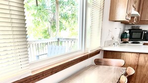 Un comedor con mesa y sillas de madera, una ventana con persianas, y una zona de cocina con microondas.