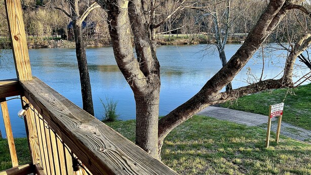 Terraza de madera con vistas a un lago, árboles y una zona verde.