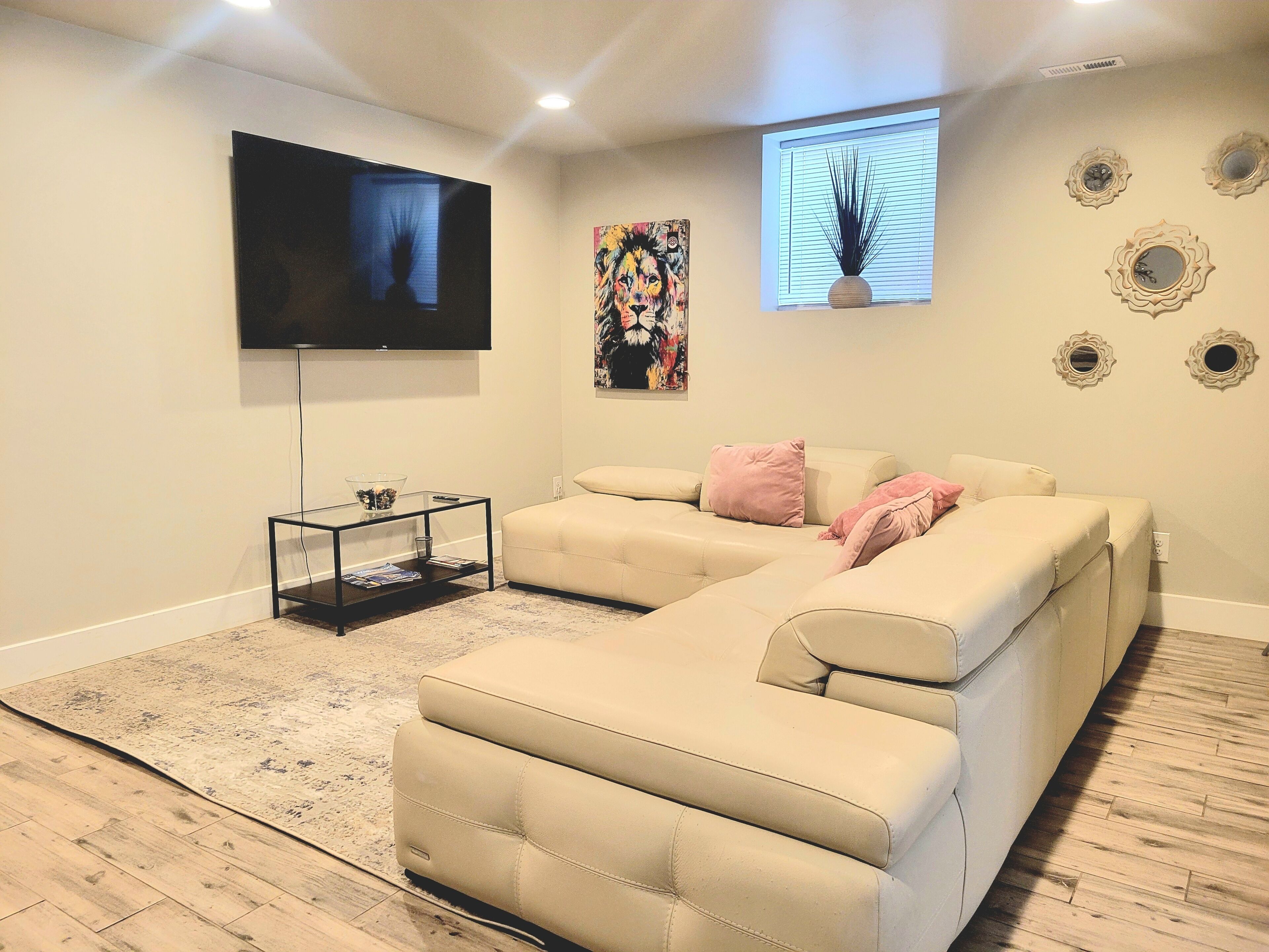 Un salon avec un canapé d’angle beige, un téléviseur à écran plat fixé au mur et une petite table d’appoint.