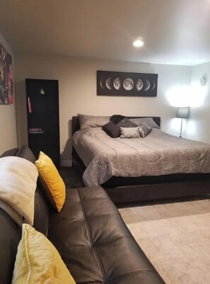 Relax in this serene bedroom with a large bed, dark leather sofa, and a unique moon phase artwork.