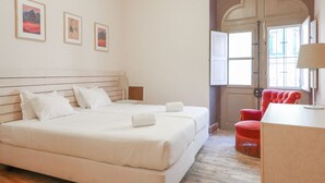 A bedroom with a large bed, a red chair, and a door with a decorative arch. - Tilia Hostel (Faro)