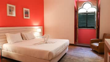 Une pièce comprenant un lit, une chaise, une fenêtre avec des volets et deux tableaux encadrés accrochés au mur.