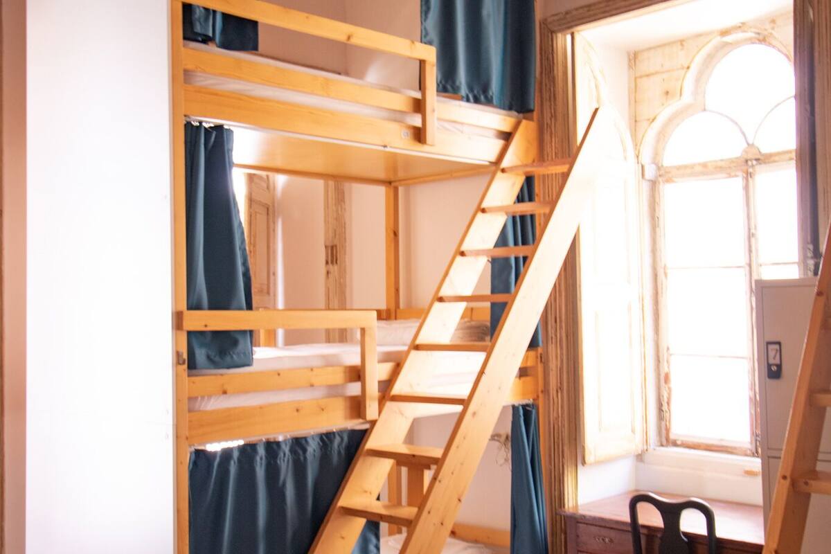 A bunk bed with a wooden ladder, a desk, and a chair in a room with wooden floors and a sloped ceiling.