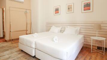 Cama de casal com roupa de cama branca, mesa de cabeceira com abajur e ar condicionado fixado na parede.