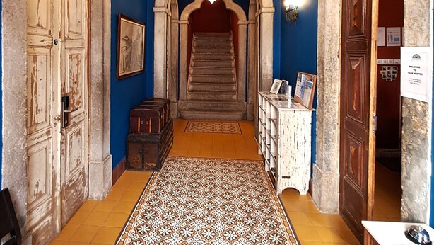 A hallway with a patterned carpet, a chandelier, and a staircase leading to an upper level. - Tilia Hostel (Faro)