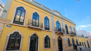 A yellow building with multiple windows and balconies, a sign indicating 'TILIA HOSTEL', and a street in front. - Tilia Hostel (Faro)