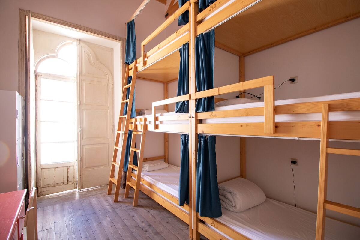 A bunk bed room with wooden frames, a ladder, and a window with curtains.