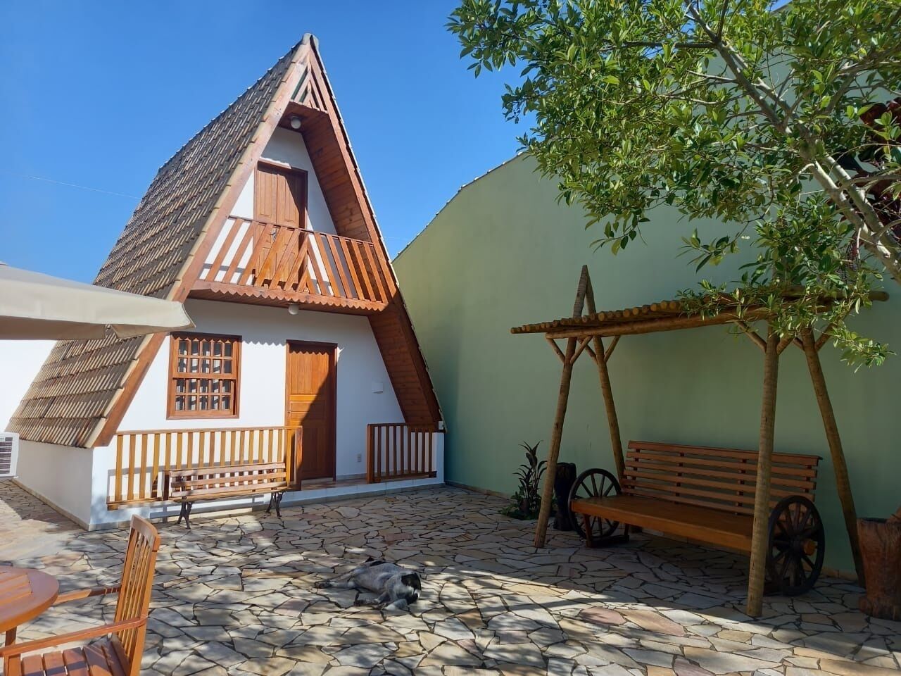 Uma casa tradicional com telhado inclinado, varanda de madeira e pátio com tijolos de pedra.