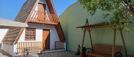 Uma casa tradicional com telhado inclinado, varanda de madeira e pátio com tijolos de pedra.
