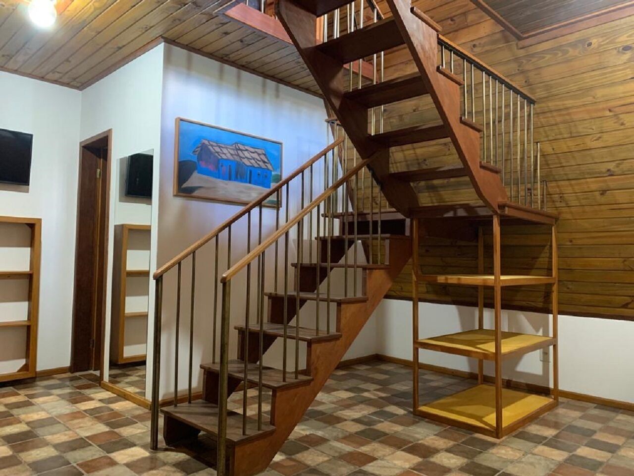 Una escalera de madera con barandilla de metal que conduce a una zona superior con estantes de madera.