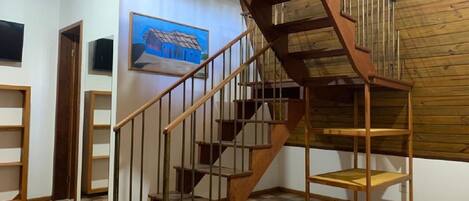 Una escalera de madera con barandilla de metal que conduce a una zona superior con estantes de madera.