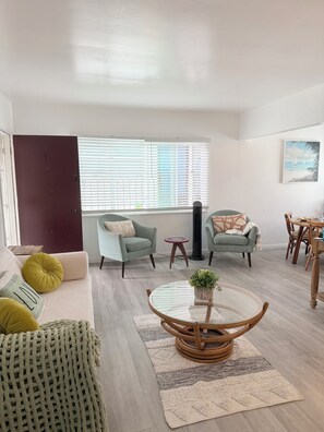 A modern living room with a sofa, two armchairs, a round coffee table, and a dining area with a table and chairs.