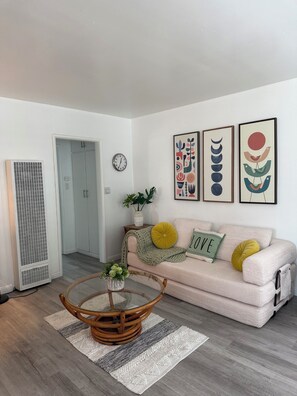 A living room with a sofa, a round coffee table, a clock, and framed artwork on the wall. - Beautiful  unit in the heart of Belmont Shores!!! (Long Beach)