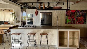 Eine moderne Küche mit einer zentralen Kochinsel, Barhocker, einem Kühlschrank und einem großen Fenster.