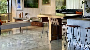 Eine moderne Küche mit einer zentralen Kochinsel, Barhocker und einer Sitzecke mit Sofa und Hocker.
