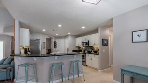 A modern kitchen with a central island, bar stools, and white cabinetry.
