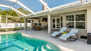 A covered outdoor swimming pool area with lounge chairs and a patio table.