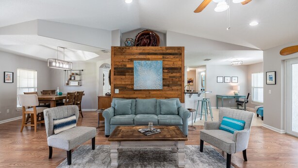 A spacious living room with a wooden accent wall, a blue sofa, two armchairs, and a coffee table.