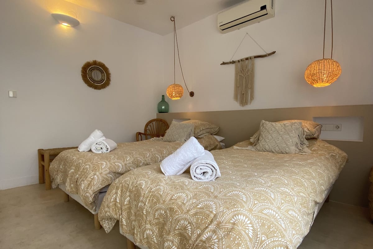 A bedroom with two beds, a ceiling fan, wall-mounted air conditioning, and decorative lighting.
