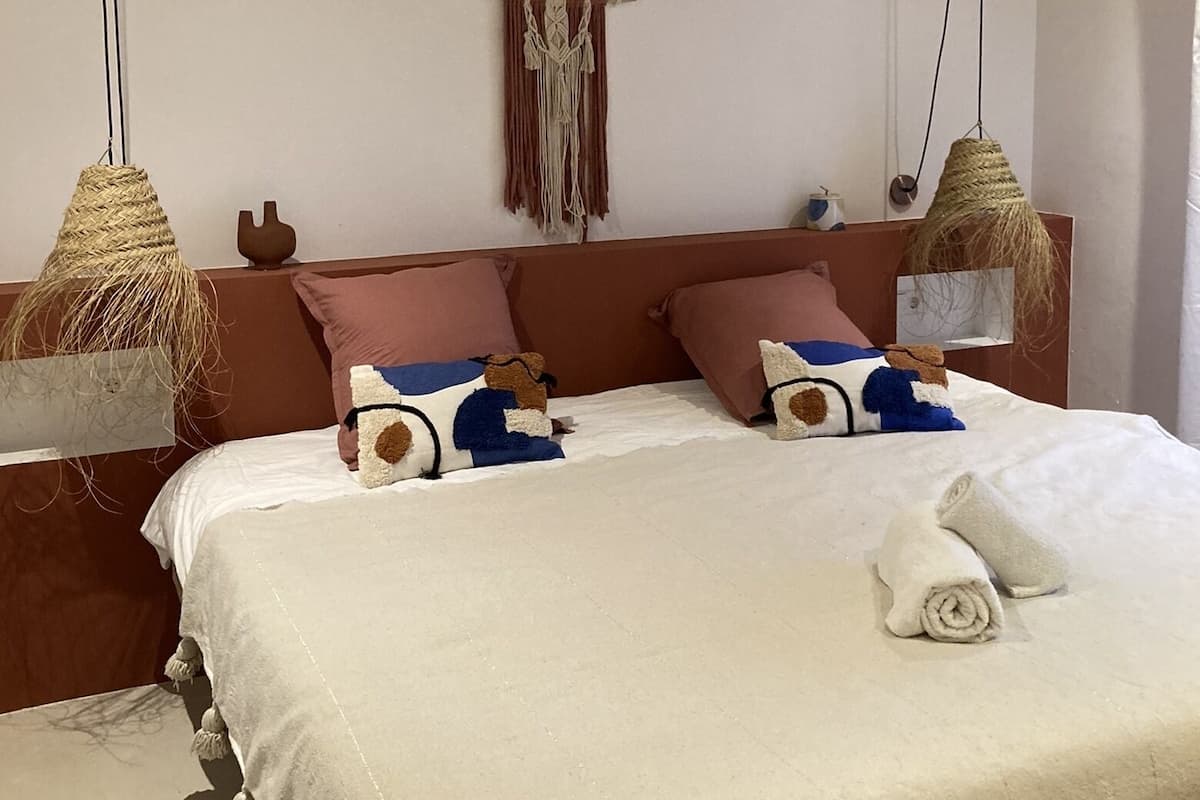 A bed with a beige bedspread, two pillows, and a rolled towel.