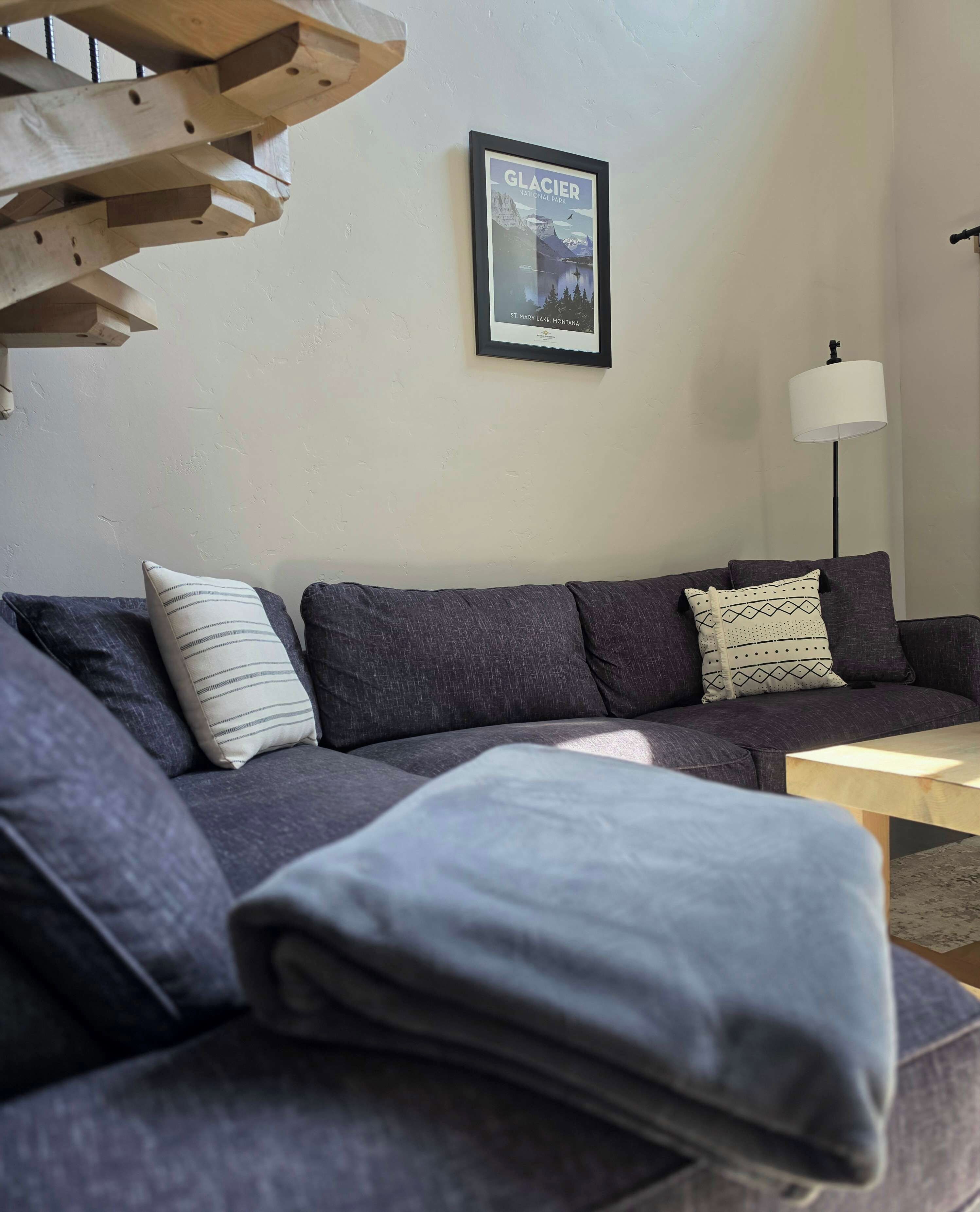 Ein modernes Wohnzimmer mit einem grauen Sofa, einem gerahmten Bild vom Glacier National Park und einer Stehlampe.