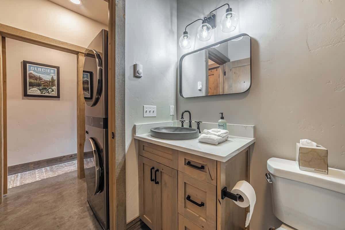 A bathroom with a wooden vanity, a sink, a mirror with lights, and a toilet.