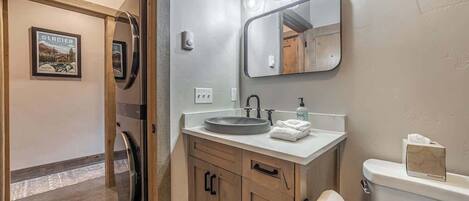A bathroom with a wooden vanity, a sink, a mirror with lights, and a toilet.