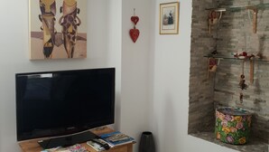 A living room with a flat-screen TV, a wooden coffee table with magazines, a framed picture on the wall, and a decorative wall shelf. - Whole house (Belvedere)