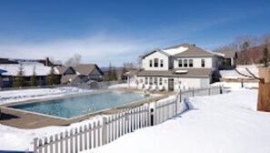 Ett stort hus med en swimmingpool, omgivet av ett vitt trästaket.