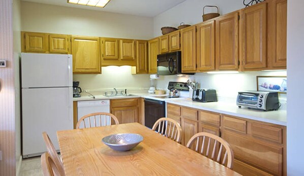 Cocina pequeña con armarios de madera, refrigerador, microondas, tostadora y una mesa de comedor con sillas.