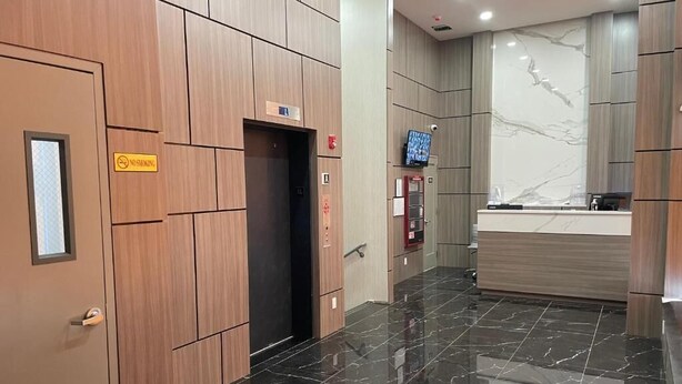 Een hotel lobby met een wand van houten panelen, een receptiebalie, een marmeren vloer en een lift.