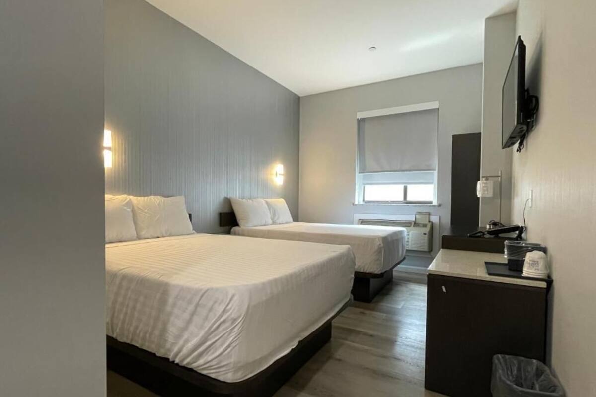 A hotel room with two beds, a desk, a TV, and a window.