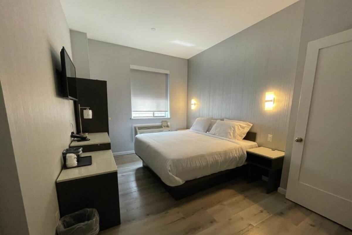 A bedroom with a bed, bedside tables, a desk, a chair, a television, and a window with blinds.