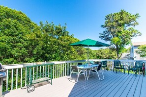 An outdoor deck with a table and chairs, a grill, and a green umbrella.