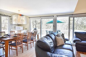 A modern living room with a leather sofa, dining table, chairs, and a kitchen area with a microwave.