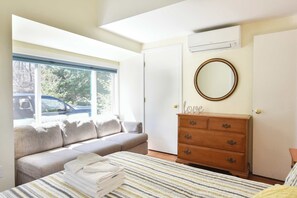 A bedroom with a bed, a dresser, a window with a view of trees, and an air conditioning unit.