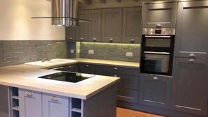 Una cucina moderna con mobili grigi, forno integrato e cappa aspirante in acciaio inossidabile.