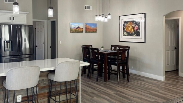 Una cocina moderna con un refrigerador de acero inoxidable, una encimera blanca y una zona de comedor con una mesa y sillas de madera.
