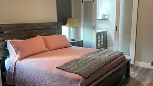 Un dormitorio con cama, cabecero de madera, ventilador de techo, mesita de noche, lámpara y puerta corredera.