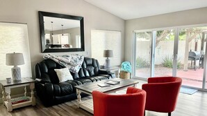 Una sala de estar moderna con un sofá de cuero negro, sillones rojos, una mesa de centro y un espejo grande.