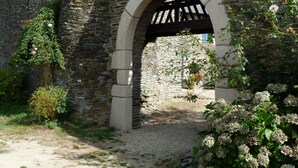 Una estructura de piedra en arco con un camino de grava que la atraviesa, rodeada de follaje y plantas con flores.