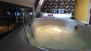 Una bañera grande con un cabezal de ducha, una cama con ropa de cama floral y una pared con estampado de floral.