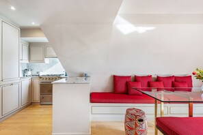 Une cuisine moderne avec des meubles blancs, un îlot central et un canapé rouge accompagné d’une table en verre.