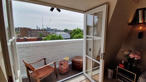 Un balcone con vista sulla città, una sedia di legno, uno sgabello decorato e una libreria piena di libri.