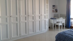 A bedroom with a large white wardrobe, a desk with a chair, and a bed with a patterned cover. - Cozy home for families in Pisa (Pisa)